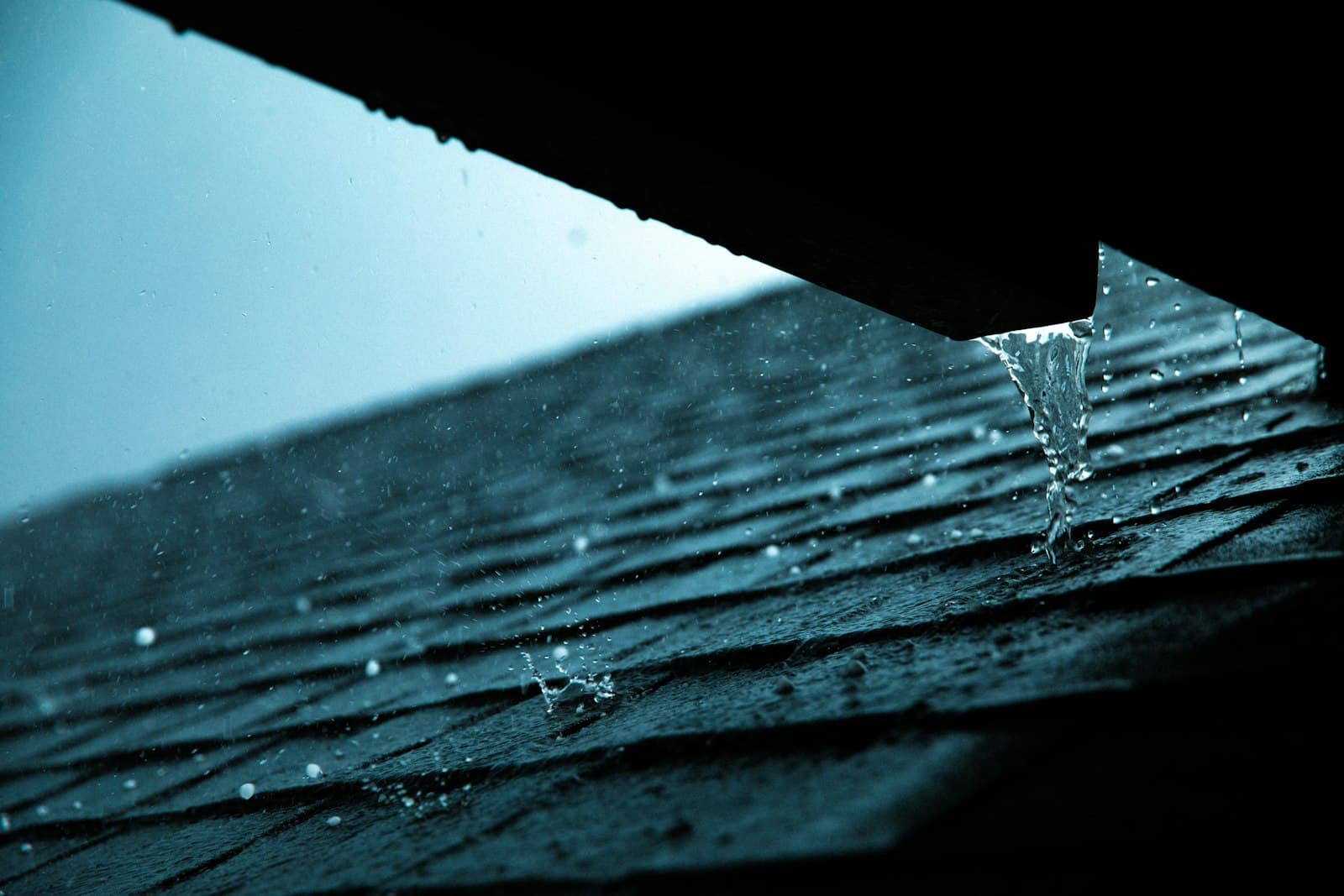 Heavy rain pouring over a roof gutter onto composition shingles